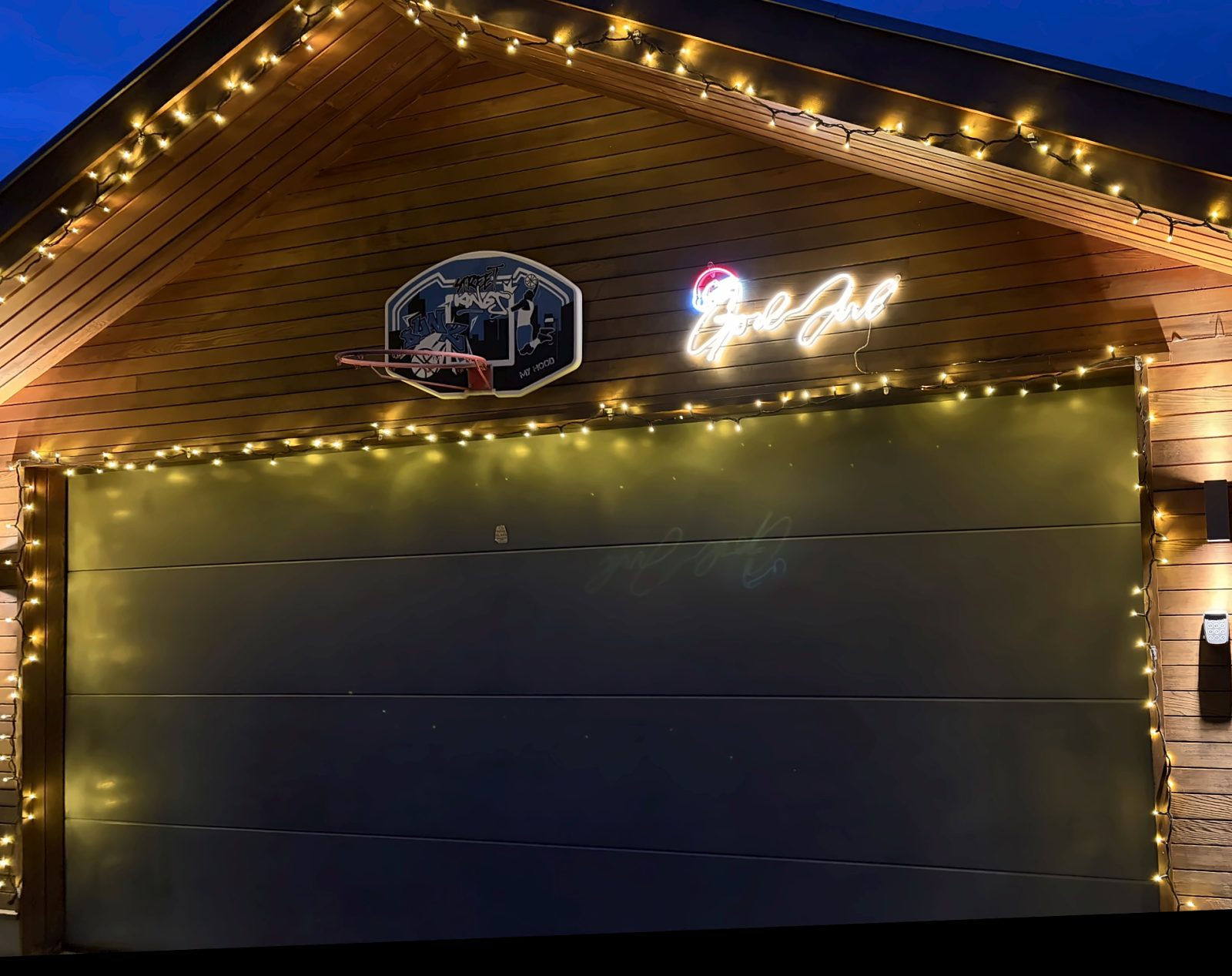 Samme garasje med lysrekker langs taket og porten og et tent God Jul-skilt