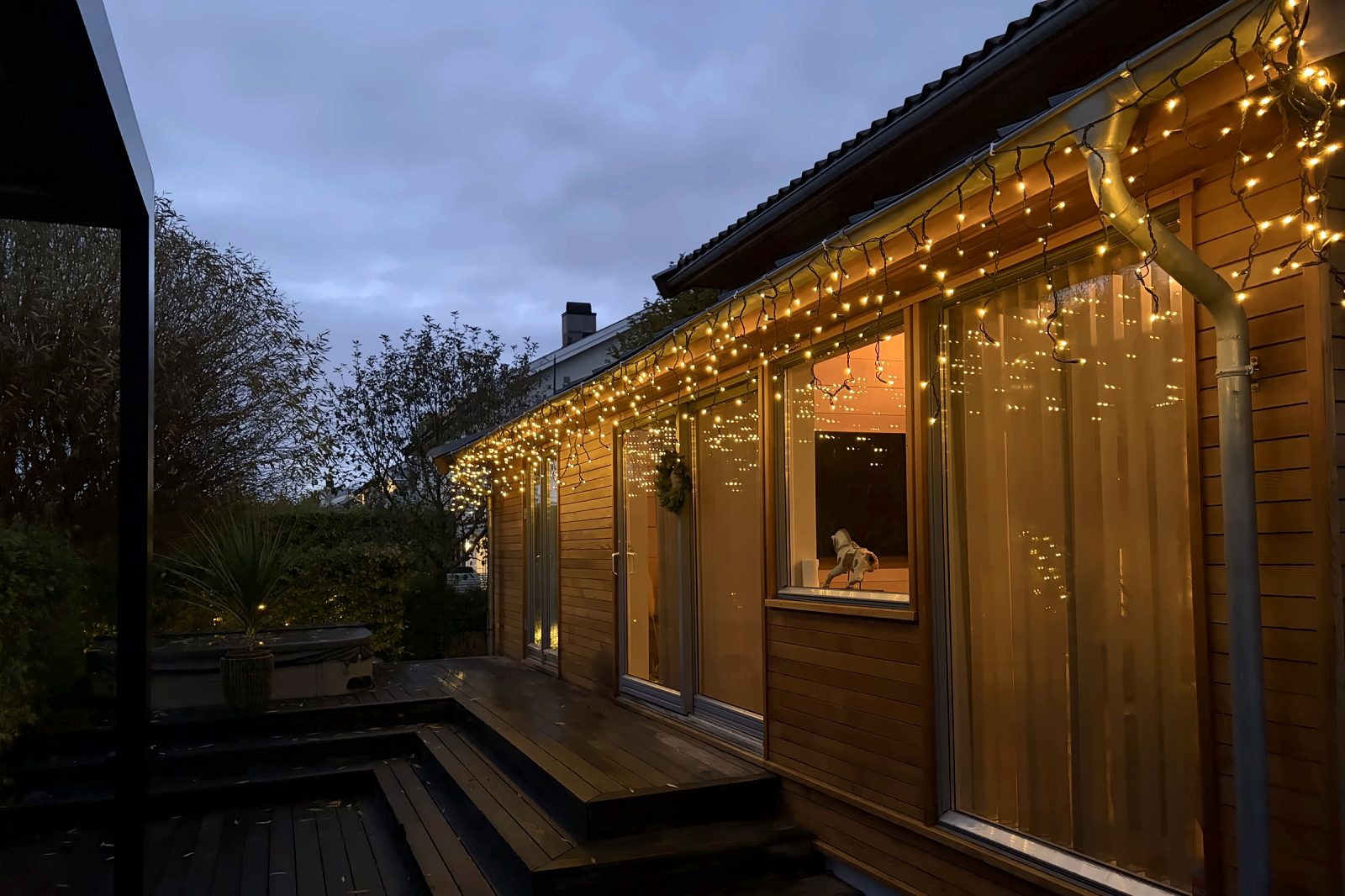 Nærbilde av istapplys under takrennen med refleksjoner i vinduene